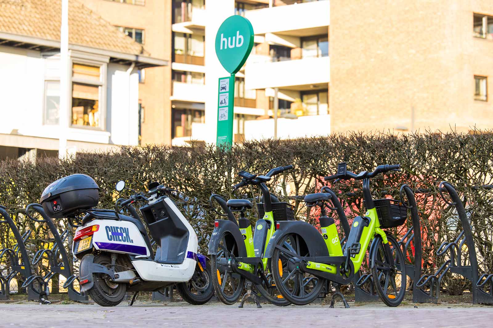 Foto van een elektrische Check-scooter en elektrische GO-fietsen aan het fietsenrek bij een deelvervoerhub aan het Wilhelminaplein in Rotterdam.