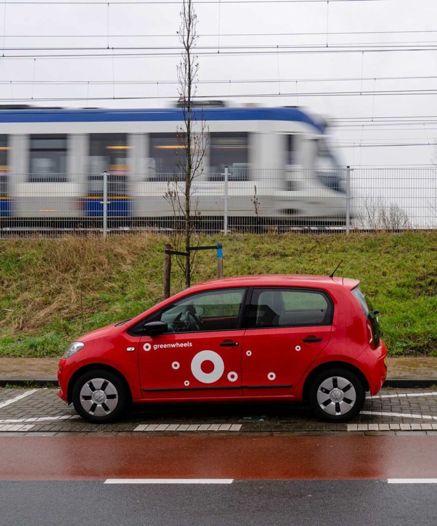 Foto van een Greenwheels-auto met op de achtergond een trein