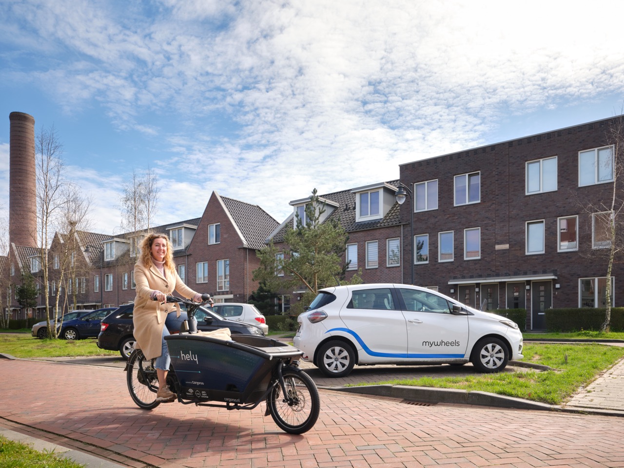 Foto van vrouw met bakfiets in woonwijk en elektrische deelauto op achtergrond