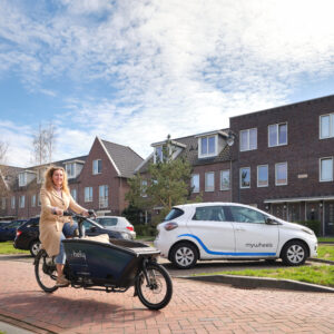 Fietser op een deelbakfiets en er is een elektrische deelauto te zien in de achtergrond