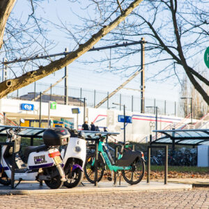 Deelmobiliteitshub bij een treinstation met geparkeerde deelscooters en deelfietsen onder een bord met het opschrift ‘hub’