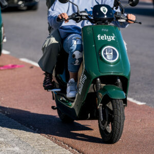 Twee personen rijden op een groene Felyx-deelscooter over een fietspad op een zonnige dag