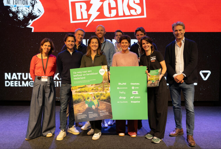 "Aanbieders van deelmobiliteit poseren op het podium met posters over duurzame en gedeelde mobiliteit tijdens een evenement"