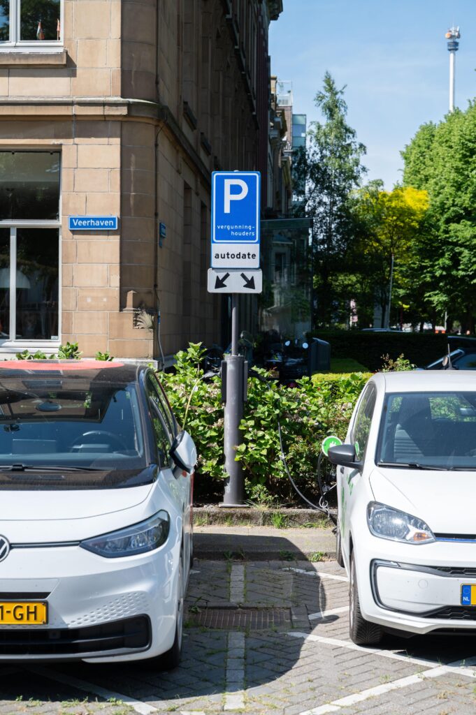 Twee elektrische deelauto’s staan geparkeerd en opladend op gereserveerde parkeervakken aan de Veerhaven, gemarkeerd met een blauw bord voor vergunninghouders en autodelen.