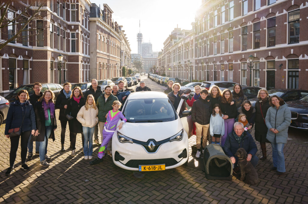 Buurtbewoners en kinderen staan samen rond een elektrische deelauto in een woonstraat.