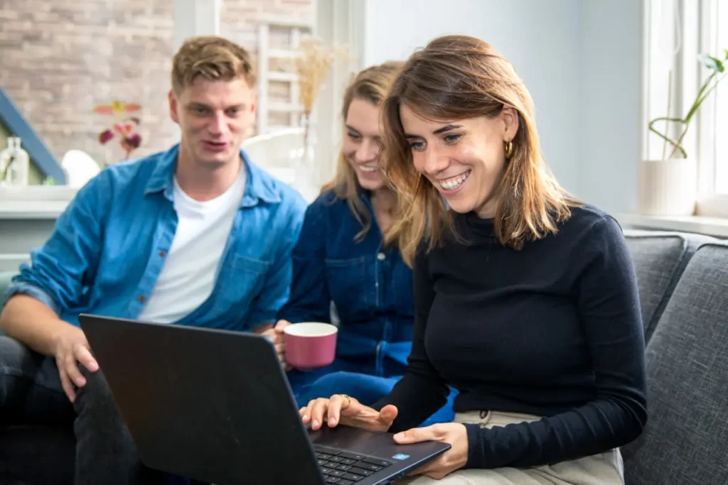 Drie mensen zitten samen op een bank en kijken naar een laptop, terwijl ze online informatie bekijken over autodelen.