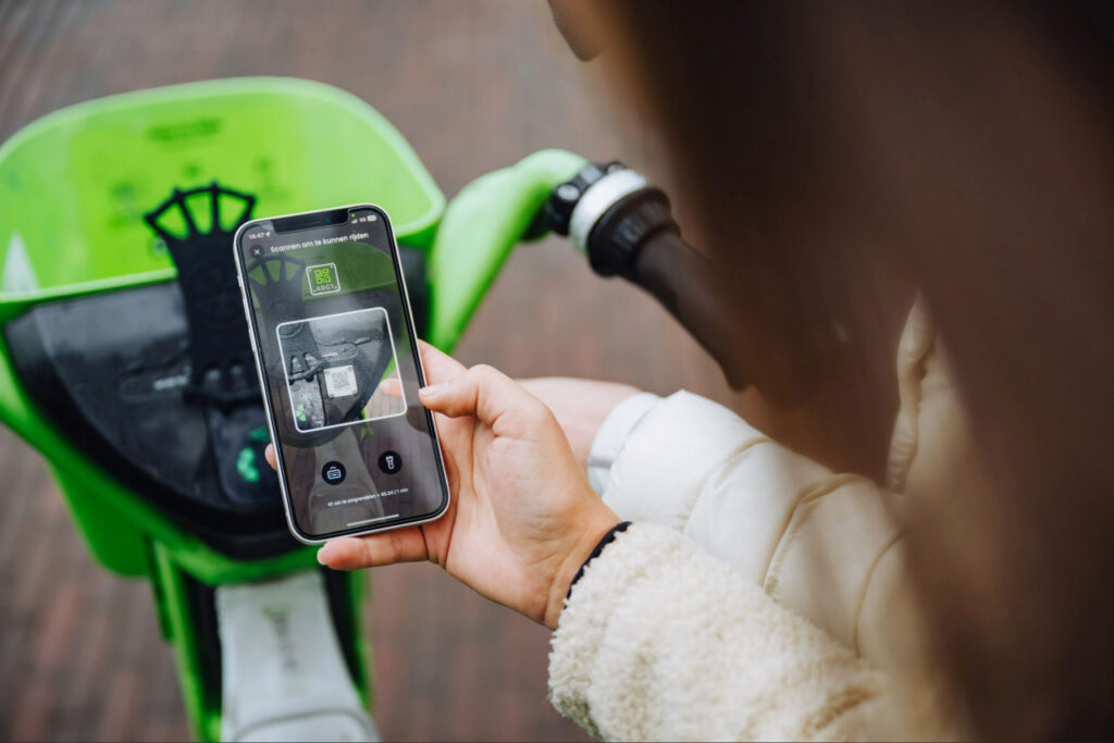Persoon scant met een smartphone een QR-code op een elektrische deelfiets om de rit te starten.