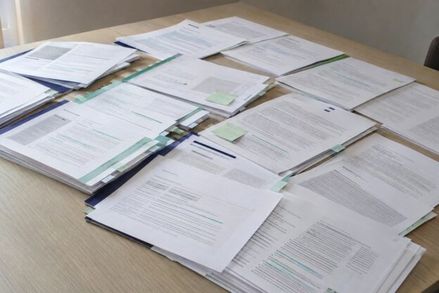 Tafel met een groot aantal deels overlappende en gemarkeerde beleidsdocumenten, klaargelegd voor vergelijking en analyse.