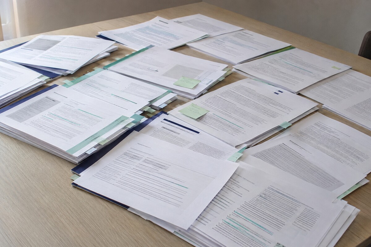 Tafel met een groot aantal deels overlappende en gemarkeerde beleidsdocumenten, klaargelegd voor vergelijking en analyse.